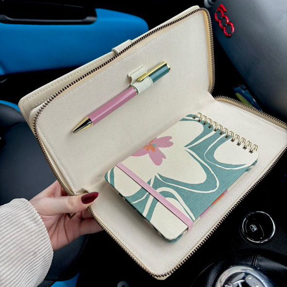 Hand holding a beige clutch with a pen and floral notebook inside, car interior background