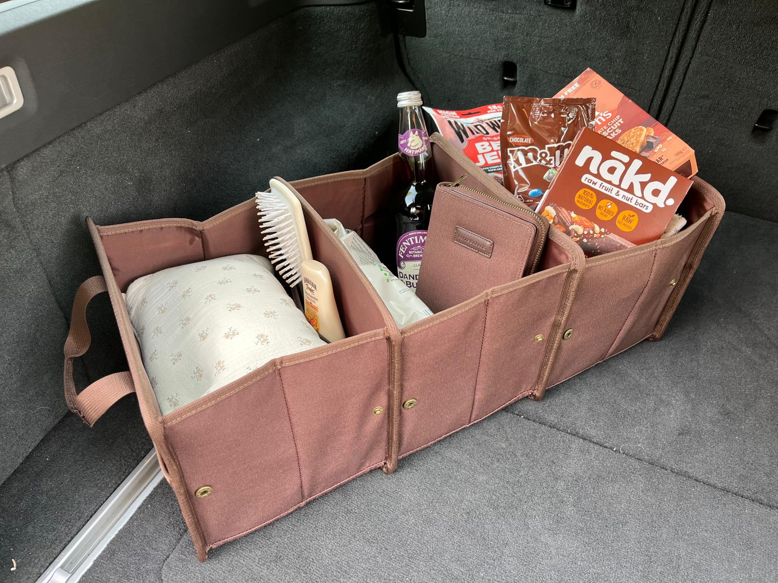 Car trunk organizer with items including a bottle, snacks, and a brush.
